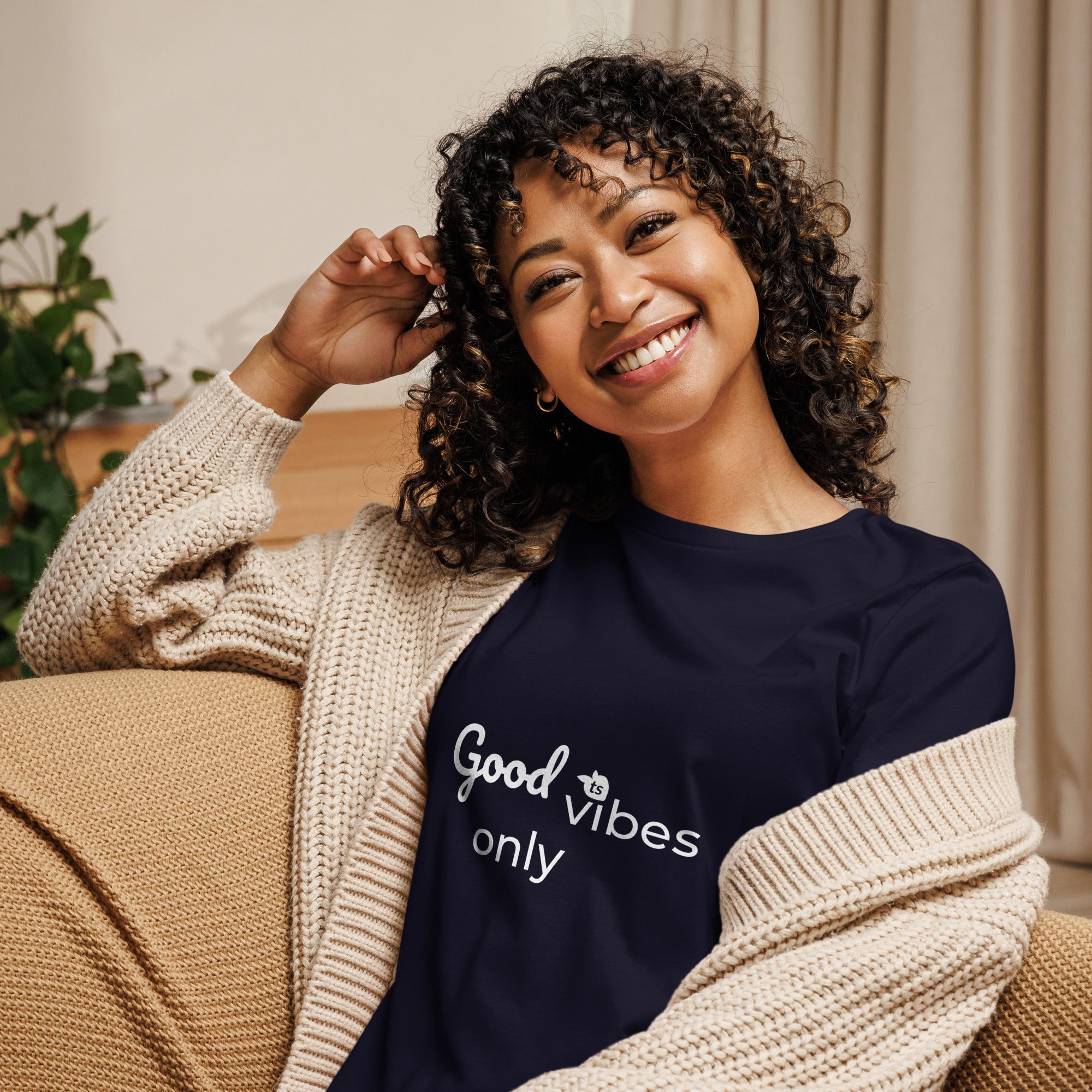 Woman wearing a black sweatshirt with 'Good vibes only' text, sitting on a couch.